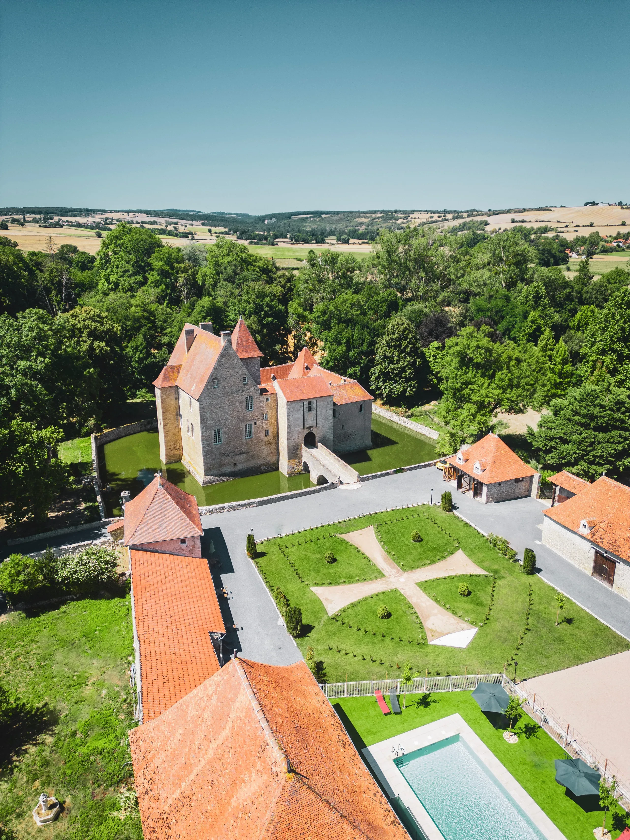 Château médiéval avec douves et jardin vue aérienne.