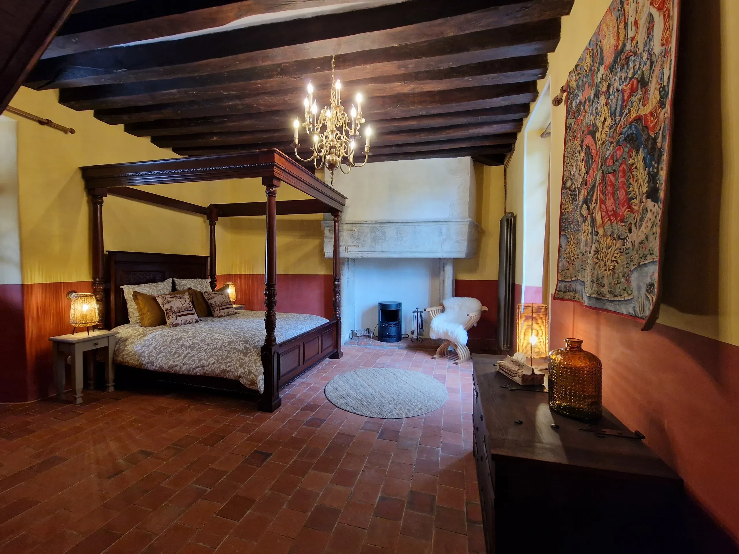 Chambre médiévale avec lit à baldaquin, cheminée et tapis.