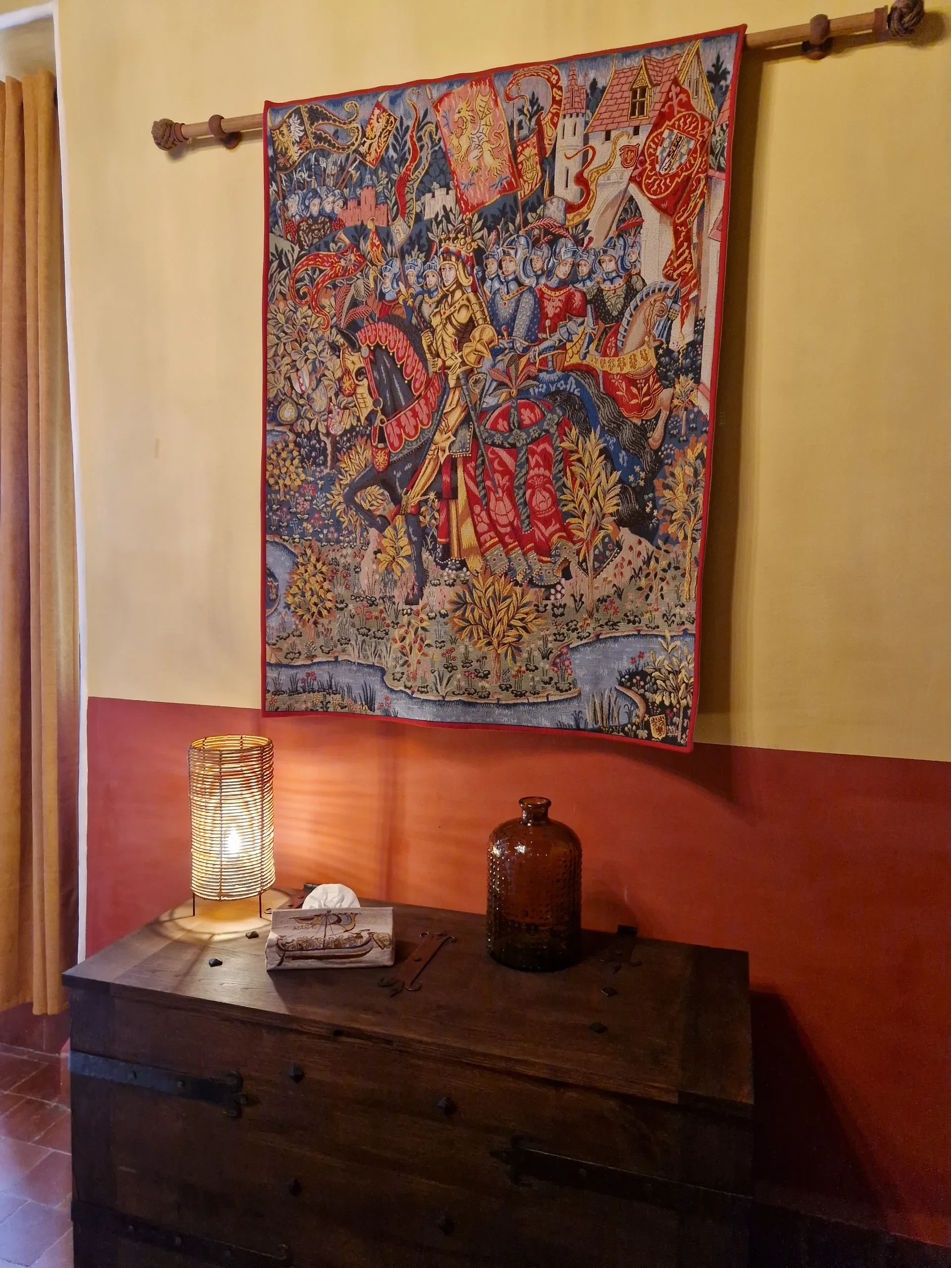 Tenture murale médiévale, lampe et coffre en bois.