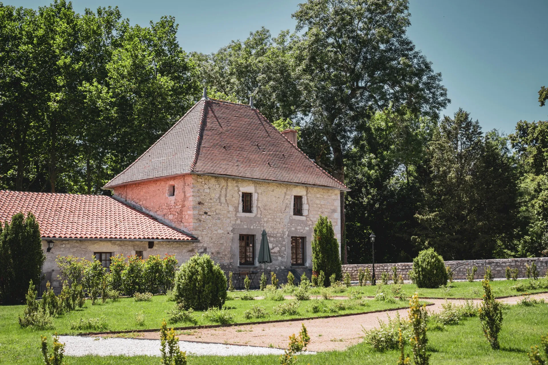 Maison en pierre dans un jardin verdoyant.