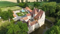 Château médiéval entouré de douves et jardins verdoyants.