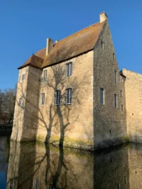 Château médiéval en pierre avec reflets sur l'eau.