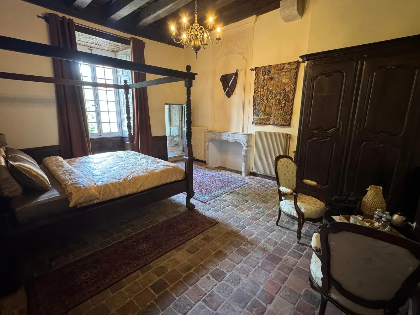 Chambre médiévale avec lit à baldaquin et tapisserie.