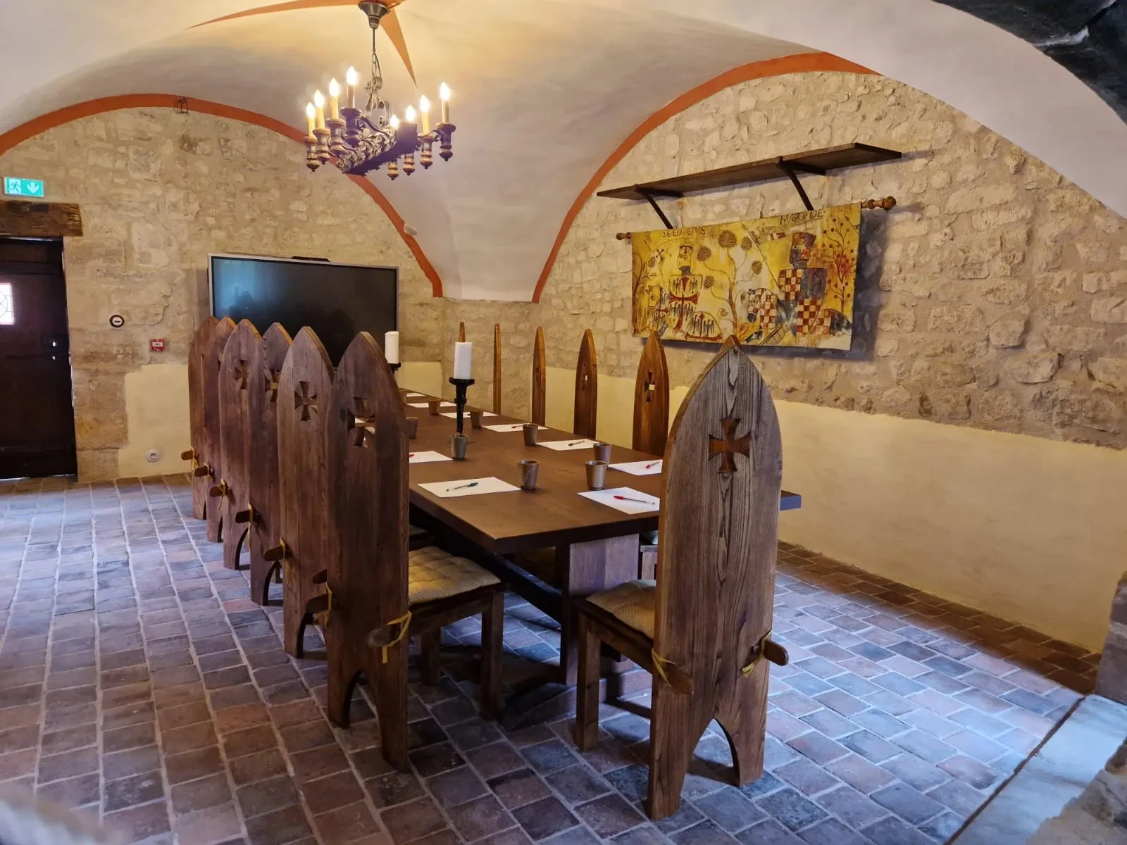 Salle médiévale avec table et chaises en bois.