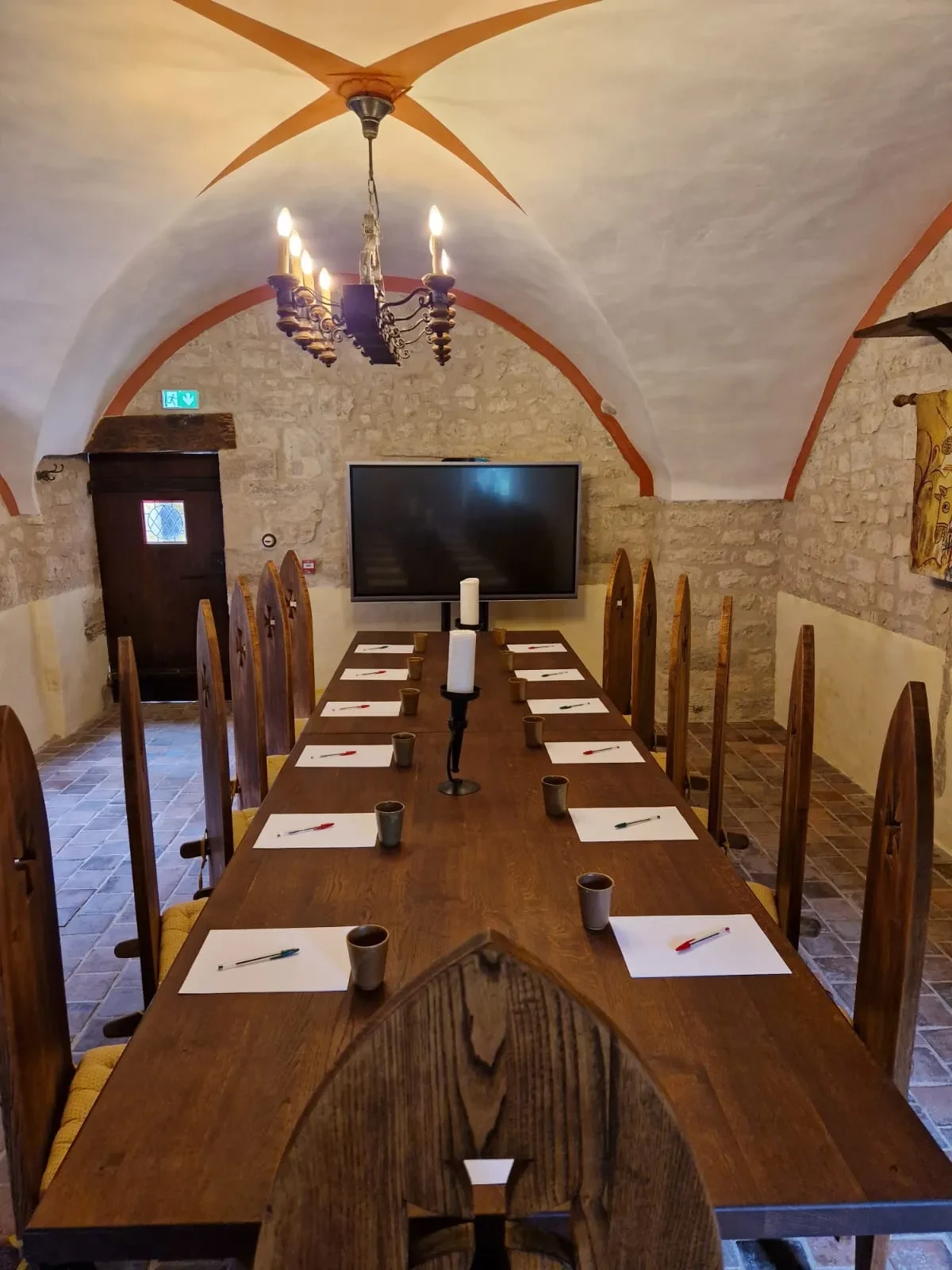 Salle de réunion médiévale avec table et chaises en bois.