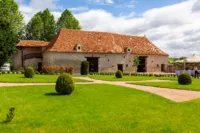 Grande grange en pierre avec jardin verdoyant.